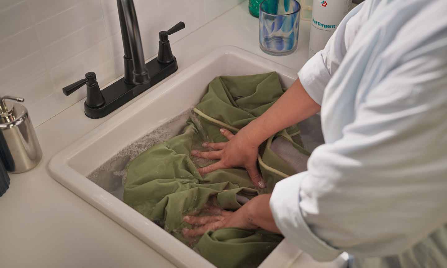 A person placing a dog bed cover and blankets into a washing machine, showing practical cleaning steps to reduce mite spread